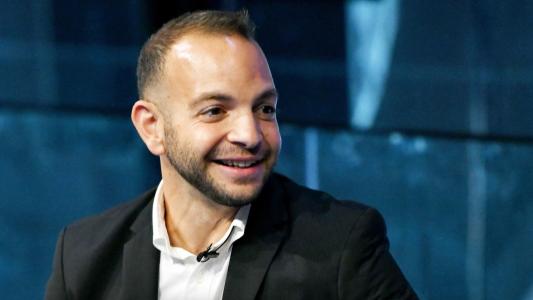 A man in a black suit and white shirt is smiling.