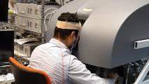 A man using a machine to control a surgical robot. Wires are connected to the back of his head.