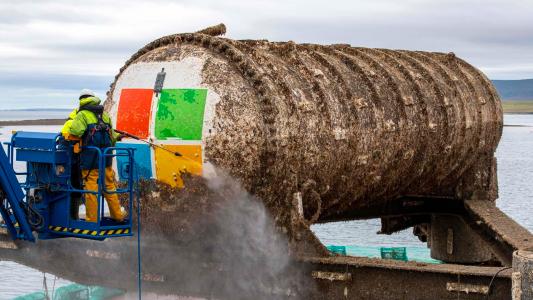 A man is spraying paint on a large barrel underwater.