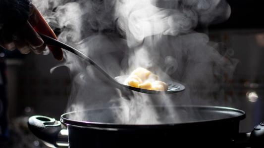 A person is holding a spoon in a pot with steam coming out of it.