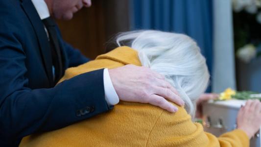 A man in a suit is hugging a woman at a funeral.